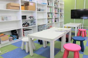 教室風景の写真です。参考書が置かれている棚の前にひざ下くらいのテーブルがあり、白・ピンク・青の可愛らしい椅子が並んでいます。